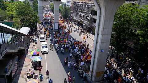 People walk in the shade of a metro rail bridge as they participate in a religious procession on a hot summer day in Hyderabad