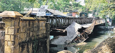 The footbridge attached to the old iron bridge in a partially collapsed state.