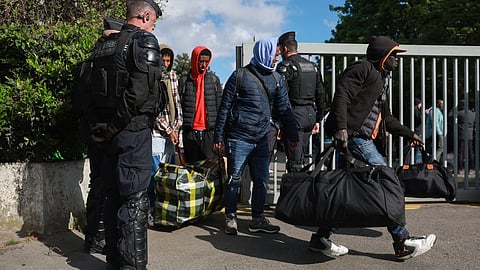 French gendarmes stand guard next to migrants leaving for another location, during the evacuation of France's biggest squat in the southern suburbs of Paris in Vitry-sur-Seine on April 17, 2024, 100 days before the Olympic Games.