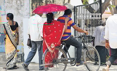 A woman seeks refuge from the sun under an umbrella on the way to a polling booth in Chennai