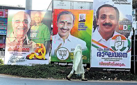A woman walks past the hoardings of candidates representing the three fronts in Ulliyeri