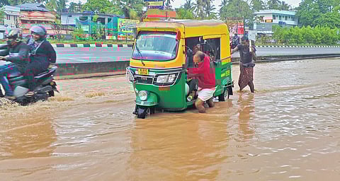 An autorickshaw driver struggles as his vehicle gets stuck in a pohole at a waterlogged road at Enchakkal Junction in Thiruvananthapuram on Wednesday