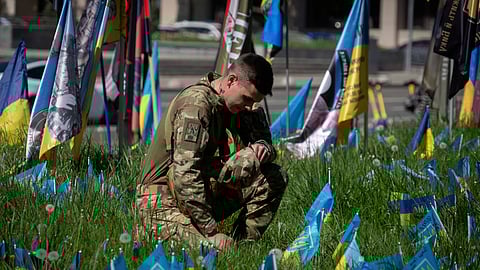 A soldier stands kneeling at the Independence square in Kyiv, Ukraine surrounded by small national flags symbolising Ukrainian soldiers killed in the war with Russia.