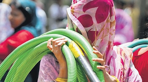 A woman carries a pipe to fetch water from a tanker amid the ongoing heatwave, at Chanakyapuri in New Delhi on Thursday