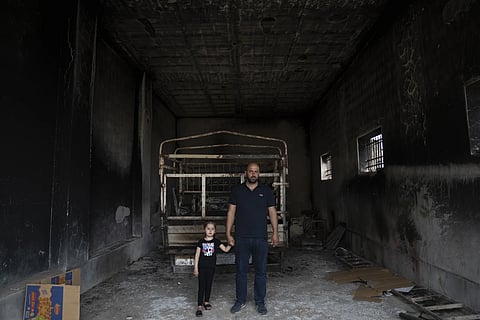 Ibrahim Dawabsha, 34, holds hands with his daughter Ghena, 3, while posing for a picture in front of his truck, at the garage of the family house, that was torched during an attack by Israel settlers last month, in the West Bank village of Duma, Tuesday, April 30, 2024.