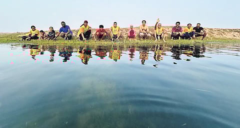 Children dive and splash in the water, while advanced swimmers prepare to cross the river, accompanied by lifeguards proficient in basic life-saving skills who retrieve plastic debris from the water.