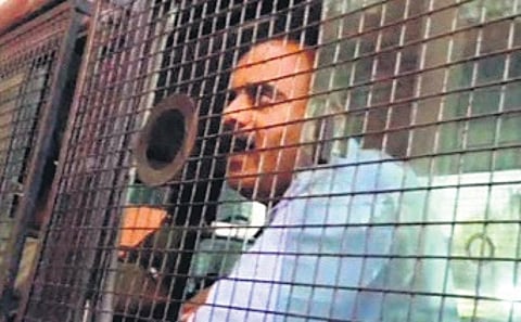 Devaraje Gowda talks to the media from a police van in Hassan on Friday