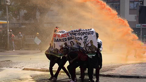 Protesters hide behind a banner as Kenya police spray water cannon at them during a protest over proposed tax hikes in a finance bill in downtown Nairobi, Kenya.
