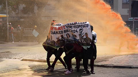 Protesters hide behind a banner as Kenya police spray water cannon at them during a protest over proposed tax hikes in a finance bill in downtown Nairobi, Kenya