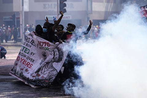 Protesters hide behind a banner as police fire tear gas at them during a protest over proposed tax hikes in a finance bill in downtown Nairobi, Kenya Tuesday.