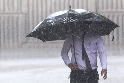 A man covers himself with an umbrella as rains lash at Begumpet in Hyderabad.