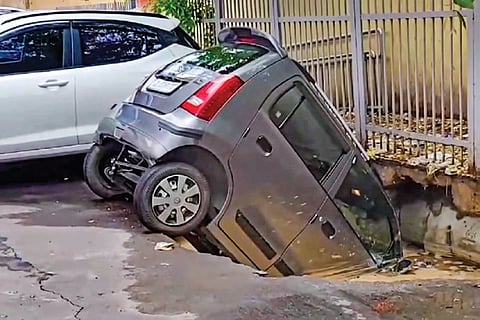 A car lies in a pothole near Rohini Sector-18 metro station after part of a road caved in following heavy rainfall