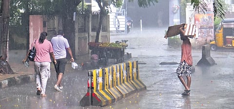 A man crosses a road using a cardboard to shield his head from the heavy downpour at Somajiguda in Hyderabad on Saturday