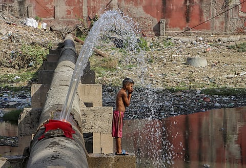 A child stands under water leaking from a broken pipeline to get relief from the scorching heat on a hot summer day in Delhi