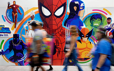 Convention attendees blur past a wall of illustrated Marvel superhero characters during preview night for Comic-Con International.