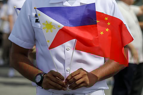 A member of the Philippine Coast Guard holds flags of the Philippines and the People's Republic of China.