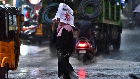A women seen crossing the road protecting her from sudden heavy rain with a makeshift cover at perumbur.
