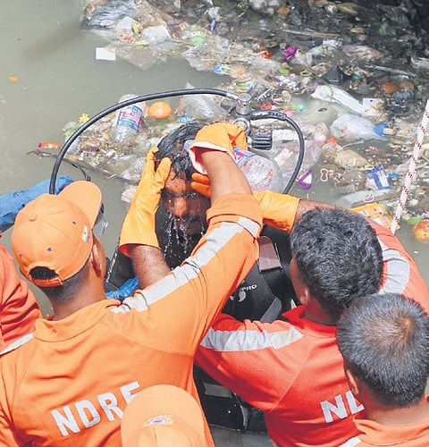NDRF personnel clean the head of a scuba diver after he emerged from the garbage-filled Amayizhanchan canal in Thiruvananthapuram