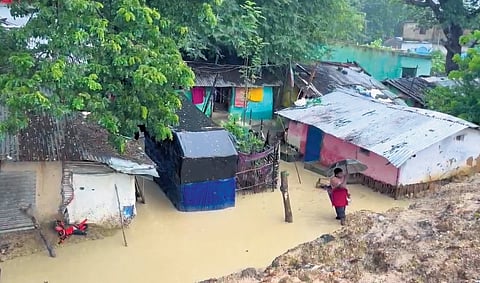 Houses flooded in a village; water flows over a bridge.