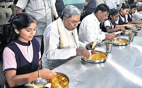 Chief Minister Siddaramaiah and Minister HC Mahadevappa have lunch with students of a residential school in Bengaluru on Friday.