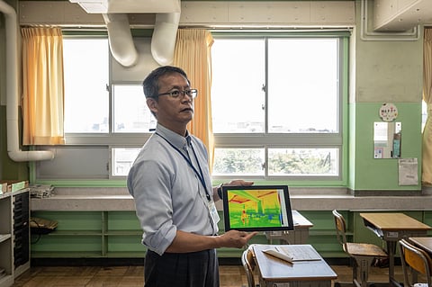 A Japanese ward official in charge of facility renovation displays an image taken with a thermal camera to show the insulating effect in a Tokyo elementary school classroom.