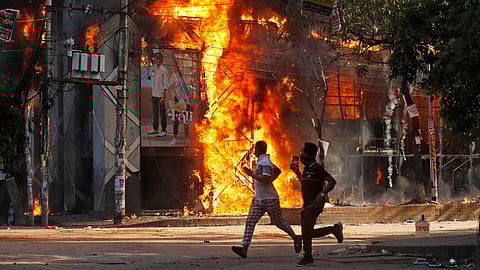 Men run past a shopping centre which was set on fire by protesters during a rally against Prime Minister Sheikh Hasina and her government demanding justice for the victims killed in the recent countrywide deadly clashes, in Dhaka, Bangladesh, Sunday, Aug. 4, 2024.
