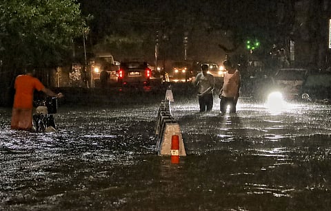 People wade through a waterlogged road during rain in Jangpura area