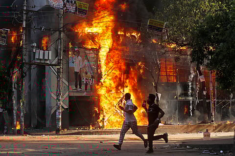 Men run past a shopping centre which was set on fire by protesters during a rally against Prime Minister Sheikh Hasina and her government demanding justice for the victims killed in the recent countrywide deadly clashes, in Dhaka