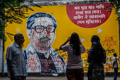 People stand and take photos in front of anti-government graffiti on a vandalised mural depicting Bangladesh's founding father, Sheikh Mujibur Rahman, days after a student-led uprising ended the 15-year rule of his daughter Sheikh Hasina, in Dhaka on August 10, 2024.