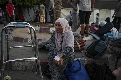 A woman sits on the curb next to her belongings outside the Al-Aqsa Martyrs Hospital in Deir al Balah, Gaza Strip, Sunday, Aug. 25, 2024.