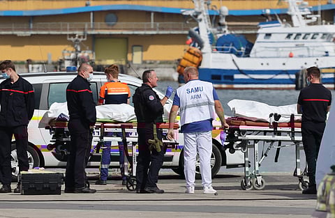Firefighters, a police officer and a doctor of the SAMU emergency unit stand next to bags containing the bodies of migrants who died after the sinking of a migrant boat attempting to cross the English Channel to England, in Boulogne-sur-Mer, northern France