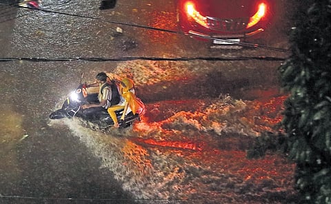 A man rides his bike amidst rain on a waterlogged road at BS Maqta in Hyderabad