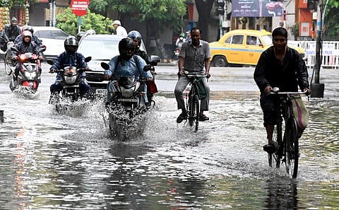 Commuters wade through a waterlogged road after rainfall, in Kolkata