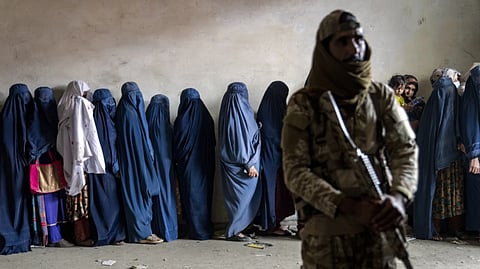 A Taliban fighter stands guard as women wait to receive food rations distributed by a humanitarian aid group in Kabul, Afghanistan, Tuesday, May 23, 2023.