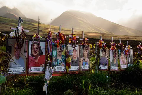 Photos of victims are displayed under white crosses at a memorial for the August 2023 wildfire victims, above the Lahaina Bypass highway, Dec. 6, 2023, in Lahaina, Hawaii.