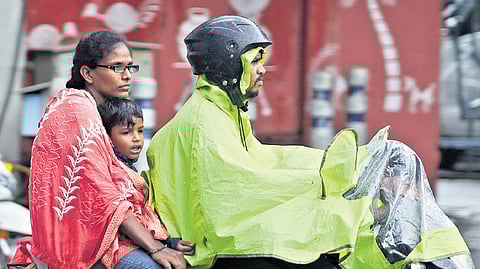 Pillion riders shield themselves with raincoat and shawl amidst rains in Hyderabad on Monday afternoon.