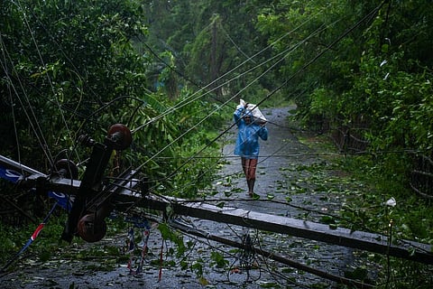 A man walks along a road that has been blocked by a fallen electricity pole after cyclone Dana made landfall at Talakrunia village in Balasore district.