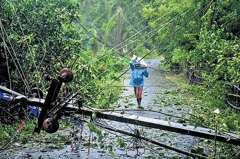A man walks along a road blocked by an uprooted electricity pole at Talakrunia in Balasore