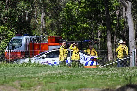 Police and firefighters stand near where three people have died after two light planes collided midair and crashed into a forested area southwest of Sydney.