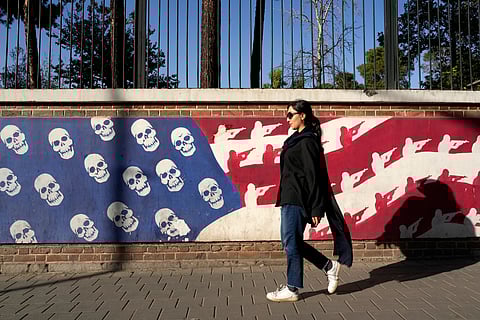 An Iranian woman walks past a satirised image of the U.S. flag on the wall of former U.S. embassy, in Tehran, Iran, Tuesday,
