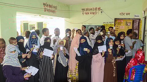 Voters show their identification cards while waiting to cast votes at a polling booth during UP's Sishamau Assembly constituency bypoll, in Kanpur.