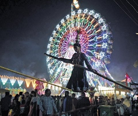 A girl walks the tightrope while the Ferris wheel rolls in the background at Balijatra.