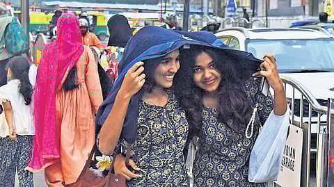 Two girls take cover under a jacket, as Bengaluru experienced an unexpected drizzle and cold spell on Tuesday evening