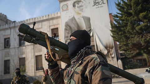 A Syrian opposition fighter holds a rocket launcher in front of the provincial government office, where an image of Syrian President Bashar Assad is riddled with bullets on the facade.