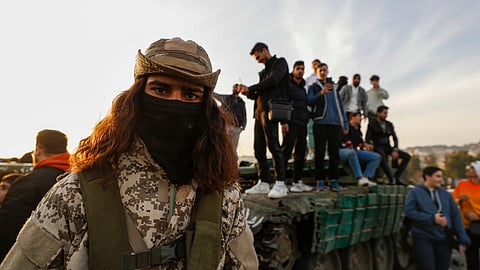 A Syrian opposition fighter, left, stands guard as Syrian citizens stand on a government forces tank, that was left on a street, during the third day of the take over of the city by the insurgents in Damascus, Syria.