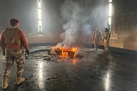 Rebel fighters stand next to the burning gravesite of Syria's late president Hafez al-Assad at his mausoleum in the family's ancestral village of Qardaha in the western Latakia province on December 11, 2024, after it was stormed by opposition factions.