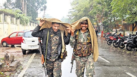 Two security personnel cover themselves as rain hits Bhubaneswar on Friday