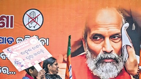 Protesters walk past a poster as BJP leaders and members protest in Bhubaneswar against alleged assault on MP Pratap Chandra Sarangi.