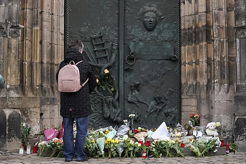 A person stands by flowers and candles placed outside St. John's Church near a Christmas Market, where a car drove into a crowd on Friday evening, in Magdeburg, Germany, Saturday, Dec 21, 2024.