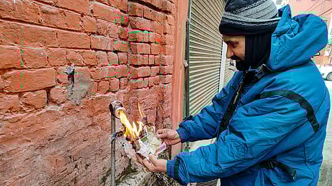 A man tries to thaw a frozen drinking water tap with the help of fire as the city recorded a minimum temperature of minus 8.5 degrees Celsius, in Srinagar, Saturday,